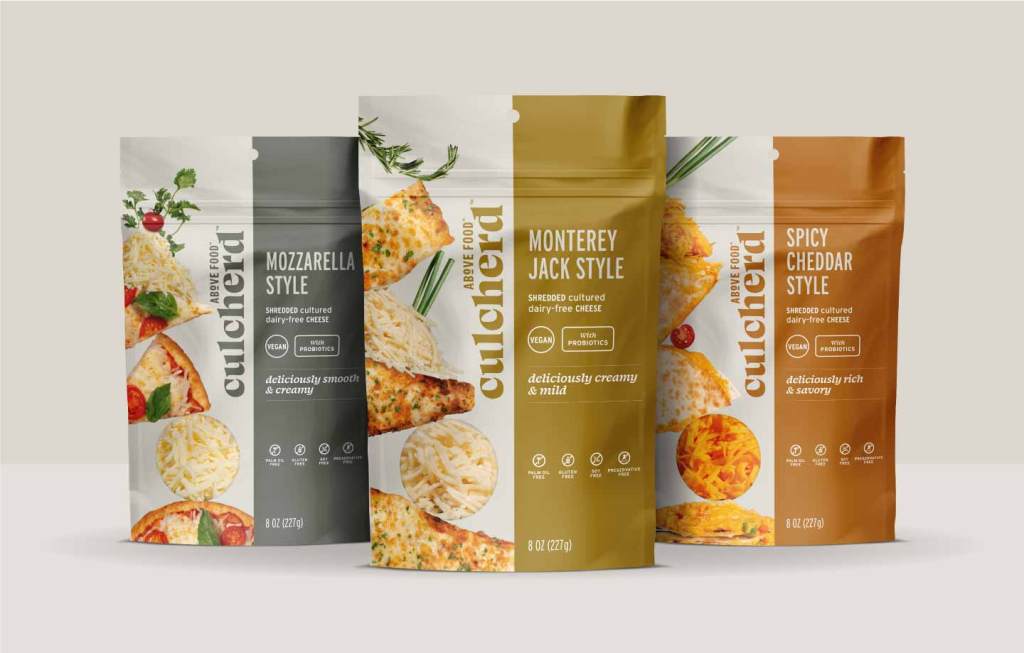 Image of three pouches of Culcherd shreds in front of a light gray background. The left pouch is a gray mozzarella-style flavor, the middle pouch is a gold-yellow monterey jack-style flavor, and the right pouch is an orange spicy cheddar-style flavor.